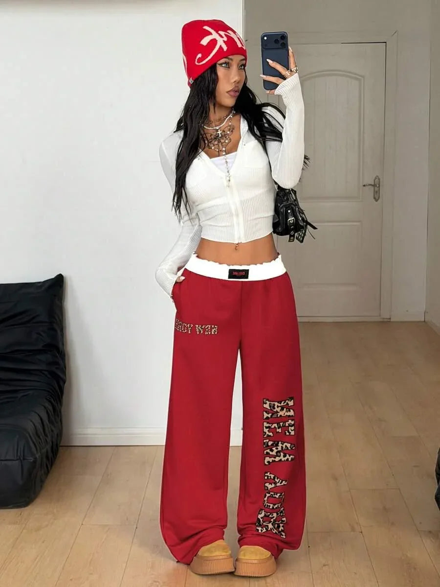Woman wearing red HUSTLE801 That Girl beanie, red cotton sweatpants, white knit zip hoodie.