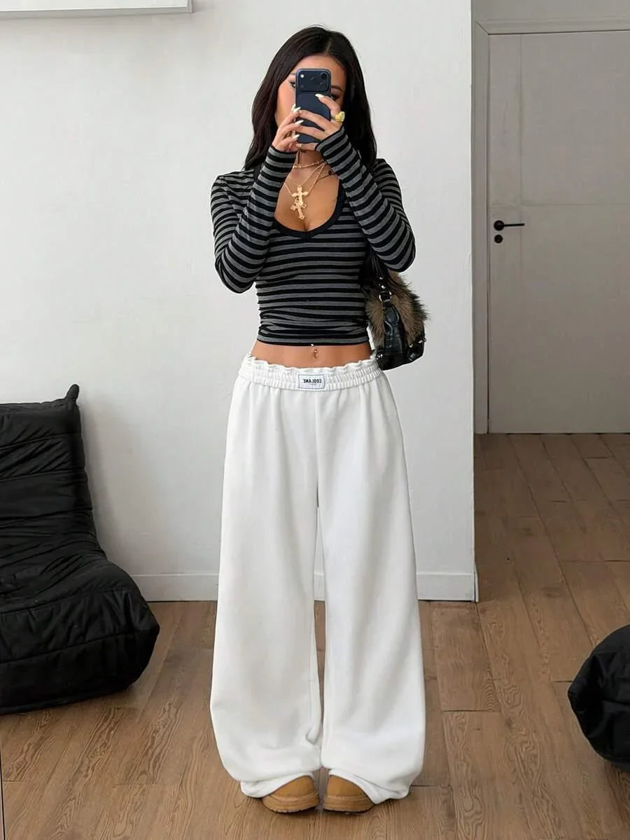 Woman wears HUSTLE801 Cool Bae white cotton baggy sweatpants and black striped top indoors