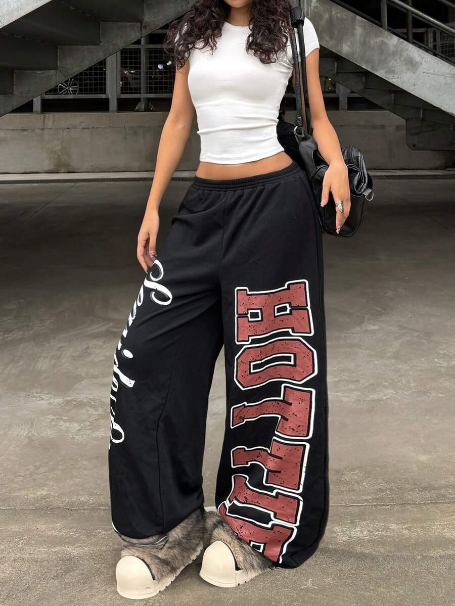 Woman in black cotton HUSTLE801 HOLLYWOOD baggy sweatpants with red lettering, urban streetwear style